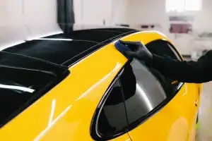A person wearing a black glove is polishing the roof edge of a shiny yellow car in a well-lit garage, showcasing professional mobile car detailing in Hillsborough County, FL.